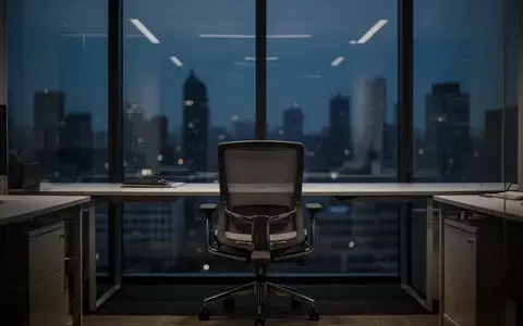 Ein leerer Büroarbeitsplatz vor einer dunklen Fensterfront mit Blick auf eine verschwommene Stadt bei Dämmerung. - Foto: über boerse-global.de