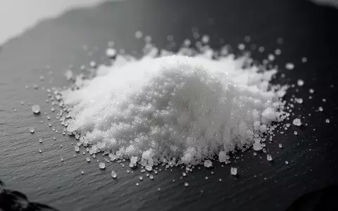 Weiße Zuckeraustauschstoff-Kristalle auf einer dunklen Schieferplatte vor einem verschwommenen Hintergrund. - Foto: über boerse-global.de