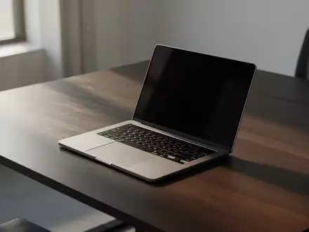 Ein moderner, minimalistischer Arbeitsplatz mit einem Laptop auf einem dunklen Holztisch bei natürlichem Tageslicht. - Foto: über boerse-global.de
