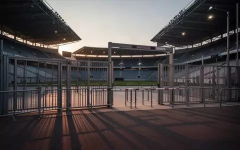Leerer Eingangsbereich eines modernen Stadions mit Sicherheitsbarrieren und Metallzäunen bei Dämmerung. - Foto: über boerse-global.de