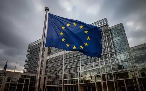 Die Flagge der Europäischen Union weht vor einem modernen Bürogebäude in Brüssel bei bewölktem Himmel. - Foto: über boerse-global.de