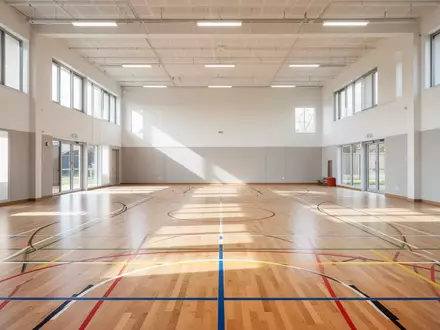 Leere Sporthalle einer Grundschule mit hellem Holzboden und markierten Spielfeldern bei Tageslicht. - Foto: über boerse-global.de