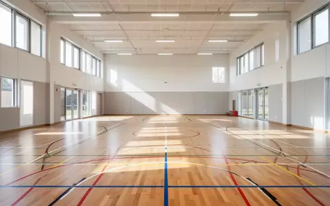 Leere Sporthalle einer Grundschule mit hellem Holzboden und markierten Spielfeldern bei Tageslicht. - Foto: über boerse-global.de