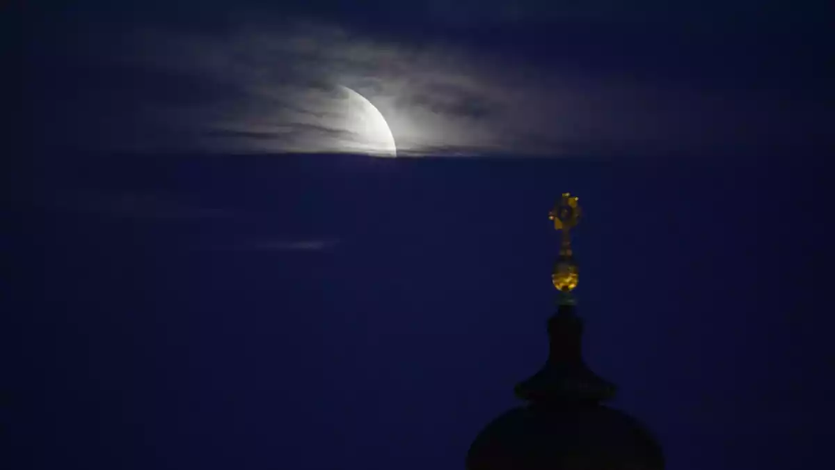 Der Mond geht am Morgen während einer partiellen Mondfinsternis hinter dem Kreuz der Frauenkirche unter.  - Bild: Robert Michael/dpa