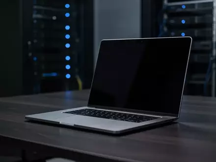 Ein minimalistischer Arbeitsplatz mit einem Laptop auf einem dunklen Holztisch in einem schwach beleuchteten Büro. - Foto: über boerse-global.de