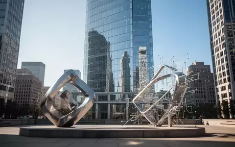 Ein modernes Hochhaus in einem Finanzviertel mit einer abstrakten Metallskulptur im Vordergrund bei Tageslicht. - Foto: ĂŒber boerse-global.de