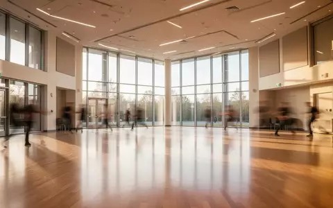 Ein lichtdurchfluteter, leerer Tanzsaal mit poliertem Parkettboden und großen Fensterfronten in einer modernen Einrichtung. - Foto: über boerse-global.de