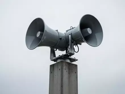 Eine moderne, auf einem Betonmast montierte Sirene vor einem bewölkten Himmel als Symbol für den Bevölkerungsschutz. - Foto: über boerse-global.de