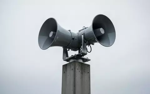 Eine moderne, auf einem Betonmast montierte Sirene vor einem bewölkten Himmel als Symbol für den Bevölkerungsschutz. - Foto: über boerse-global.de