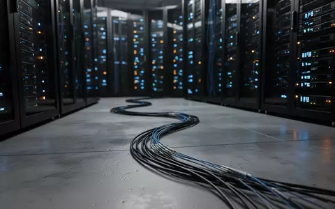 Dunkler Serverraum mit blinkenden Kontrollleuchten und einem im Vordergrund liegenden Glasfaserkabel. - Foto: über boerse-global.de