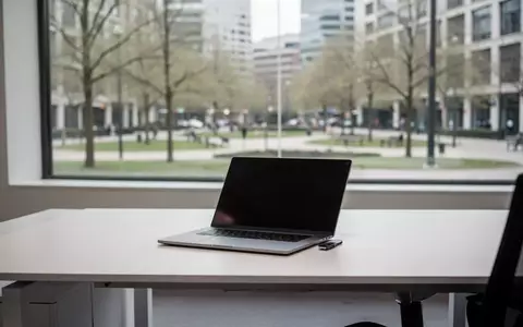 Ein minimalistischer, leerer Schreibtisch mit einem geschlossenen Laptop vor einem hellen Fenster mit Blick ins Grüne. - Foto: über boerse-global.de