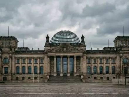 Die gläserne Kuppel des Reichstagsgebäudes in Berlin bei bewölktem Himmel. - Foto: über boerse-global.de