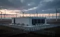 Ein modernes Rechenzentrum in einer Industrielandschaft mit Windkraftanlagen im Hintergrund bei Dämmerung. - Foto: über boerse-global.de