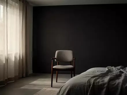 Ein minimalistisches, leer wirkendes Schlafzimmer mit einem Stuhl vor einer dunklen Wand, das eine nachdenkliche Atmosphäre erzeugt. - Foto: über boerse-global.de