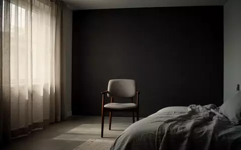Ein minimalistisches, leer wirkendes Schlafzimmer mit einem Stuhl vor einer dunklen Wand, das eine nachdenkliche Atmosphäre erzeugt. - Foto: über boerse-global.de