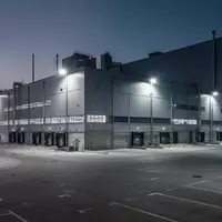 Ein weitläufiges, modernes Automobilwerk in der Dämmerung mit leeren Parkplätzen und industrieller Beleuchtung. - Foto: über boerse-global.de