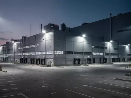 Ein weitläufiges, modernes Automobilwerk in der Dämmerung mit leeren Parkplätzen und industrieller Beleuchtung. - Foto: über boerse-global.de
