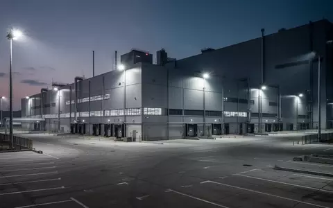 Ein weitläufiges, modernes Automobilwerk in der Dämmerung mit leeren Parkplätzen und industrieller Beleuchtung. - Foto: über boerse-global.de