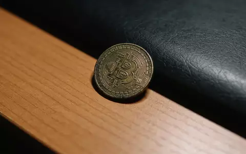 Ein einzelner Bitcoin-Token liegt einsam auf einem dunklen Schreibtisch in einem schummrig beleuchteten Raum. - Foto: über boerse-global.de