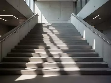 Ein leeres, modern gestaltetes Treppenhaus mit natürlichem Lichteinfall und geometrischen Schatten auf den Stufen. - Foto: über boerse-global.de