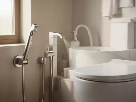Moderne, minimalistische Badezimmerarmatur mit einer Po-Dusche neben einer weißen Keramiktoilette in hellem Licht. - Foto: über boerse-global.de