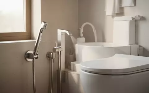 Moderne, minimalistische Badezimmerarmatur mit einer Po-Dusche neben einer weißen Keramiktoilette in hellem Licht. - Foto: über boerse-global.de