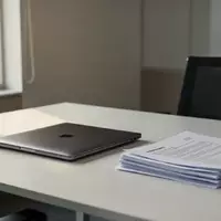 Ein aufgeräumter Schreibtisch mit einem zugeklappten Laptop und Dokumenten in einem modernen Büro bei natürlichem Tageslicht. - Foto: über boerse-global.de