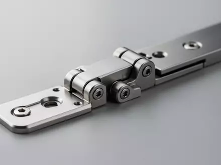 Nahaufnahme eines präzisionsgefertigten Scharniermechanismus aus Metall auf einer neutralen Oberfläche. - Foto: über boerse-global.de