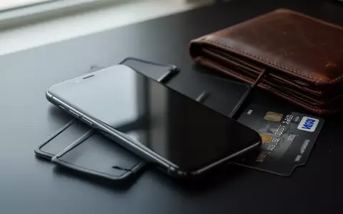 Ein Smartphone mit ausgeschaltetem Bildschirm liegt neben einer Geldbörse auf einem Schreibtisch als Symbol für digitale Sicherheit. - Foto: über boerse-global.de