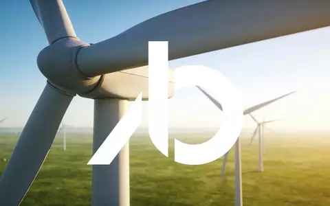 Moderne Windkraftanlagen in einer weitläufigen, grünen Landschaft bei klarem Himmel. - Foto: über boerse-global.de