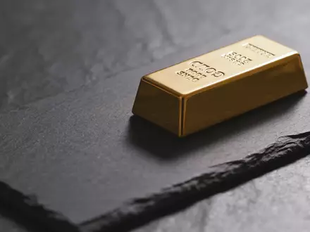 Ein einzelner Goldbarren auf einer dunklen, texturierten Oberfläche in gedämpftem, professionellem Licht. - Foto: über boerse-global.de