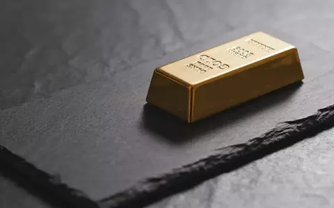 Ein einzelner Goldbarren auf einer dunklen, texturierten Oberfläche in gedämpftem, professionellem Licht. - Foto: über boerse-global.de