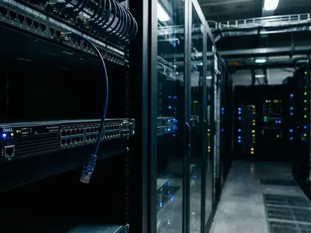 Ein Serverraum mit blinkenden Lichtern an Netzwerkschränken, wobei ein Ethernet-Kabel lose aus einem Switch hängt. - Foto: über boerse-global.de