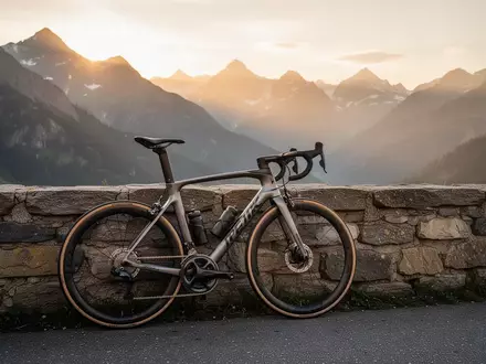 Ein professionelles Rennrad lehnt an einer Steinmauer in einer alpinen Gebirgslandschaft bei Sonnenaufgang. - Foto: über boerse-global.de