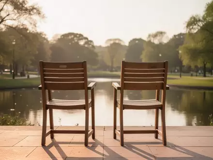 Zwei leere Holzstühle auf einer sonnigen Terrasse mit Blick in einen Park als Symbol für soziale Bindungen. - Foto: über boerse-global.de