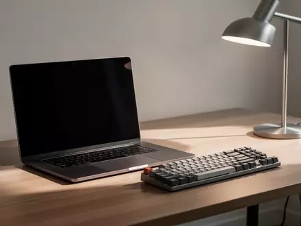 Ein minimalistischer Arbeitsplatz mit einem Laptop mit dunklem Bildschirm und einer mechanischen Tastatur auf einem Holztisch. - Foto: über boerse-global.de