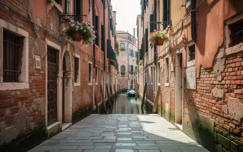 Eine leere, schmale Gasse in Venedig bei Tageslicht mit historischen Backsteinfassaden und Blick auf einen Kanal. - Foto: über boerse-global.de