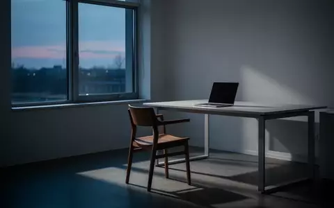 Ein minimalistischer, leerer Arbeitsplatz mit einem geschlossenen Laptop vor einem Fenster in der Abenddämmerung. - Foto: über boerse-global.de