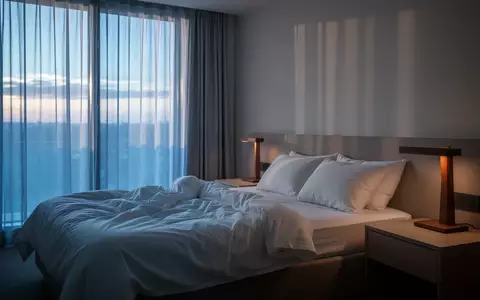 Ein minimalistisch eingerichtetes Schlafzimmer in der Morgendämmerung mit weichem Licht und einem ungemachten Bett. - Foto: über boerse-global.de