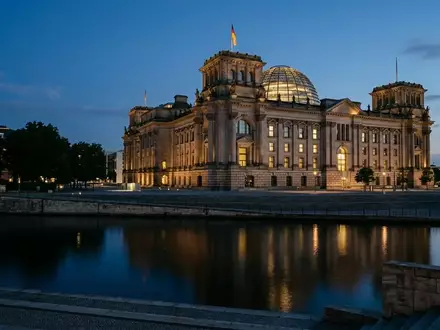 Das Reichstagsgebäude in Berlin bei Dämmerung mit beleuchteten Fenstern vor einem tiefblauen Abendhimmel. - Foto: über boerse-global.de
