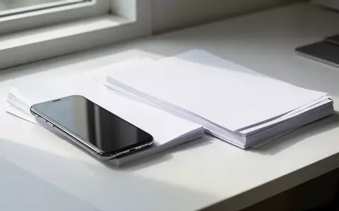 Ein Smartphone liegt neben einem Stapel weißer Papierdokumente auf einem Schreibtisch bei natürlichem Tageslicht. - Foto: über boerse-global.de