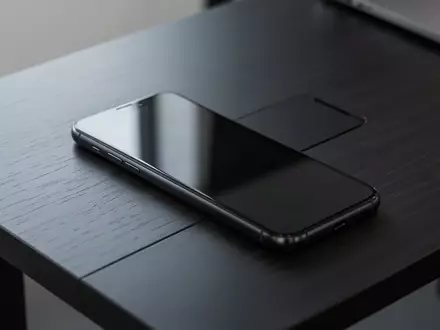 Ein dunkles Smartphone liegt auf einem hölzernen Schreibtisch, bereit für die Nutzung. - Foto: über boerse-global.de