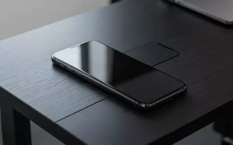 Ein dunkles Smartphone liegt auf einem hölzernen Schreibtisch, bereit für die Nutzung. - Foto: über boerse-global.de