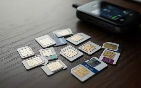 Mehrere SIM-Karten liegen auf einem dunklen Holztisch neben einem ausgeschalteten Modem-Gerät. - Foto: über boerse-global.de