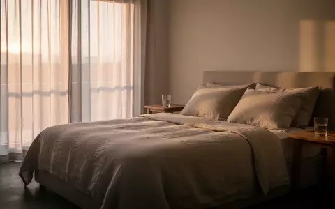 Ein minimalistisch eingerichtetes Schlafzimmer in sanftem Morgenlicht mit einem ordentlich gemachten Bett. - Foto: über boerse-global.de