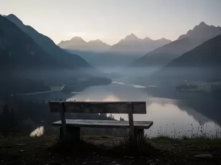 Eine minimalistische, ruhige Berglandschaft in der Abenddämmerung mit einer einsamen Holzbank mit Blick auf ein nebliges Tal. - Foto: über boerse-global.de