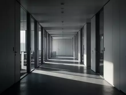 Ein leerer, kühler Büroflur mit langen Schatten und minimalistischer Architektur. - Foto: über boerse-global.de