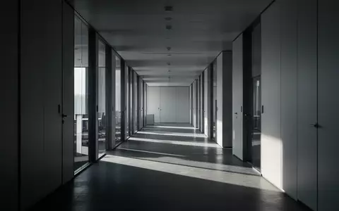 Ein leerer, kühler Büroflur mit langen Schatten und minimalistischer Architektur. - Foto: über boerse-global.de