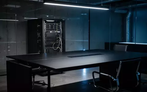 Ein minimalistisches, dunkel beleuchtetes Büro mit einem Server-Rack im Hintergrund, das eine technologische Atmosphäre vermittelt. - Foto: über boerse-global.de