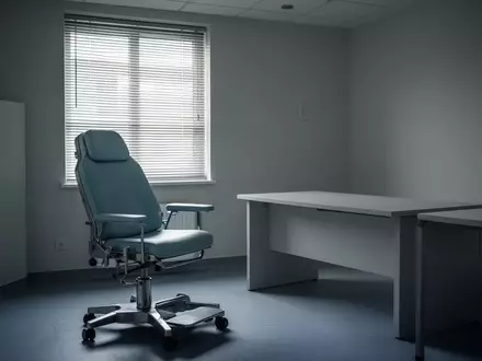 Ein leeres, klinisch wirkendes Behandlungszimmer mit einem medizinischen Stuhl in gedimmtem Licht. - Foto: über boerse-global.de